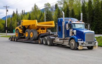 Big truck with a low platform trailer carrying a tipper truck on a public parking area of a truck stop